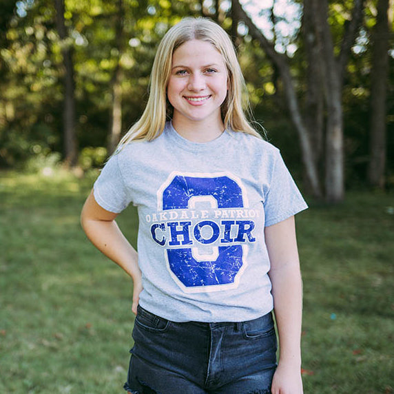 Girl stands in field wearing a light gray tshirt that reads, "Oakdale Patriot Choir" on it.