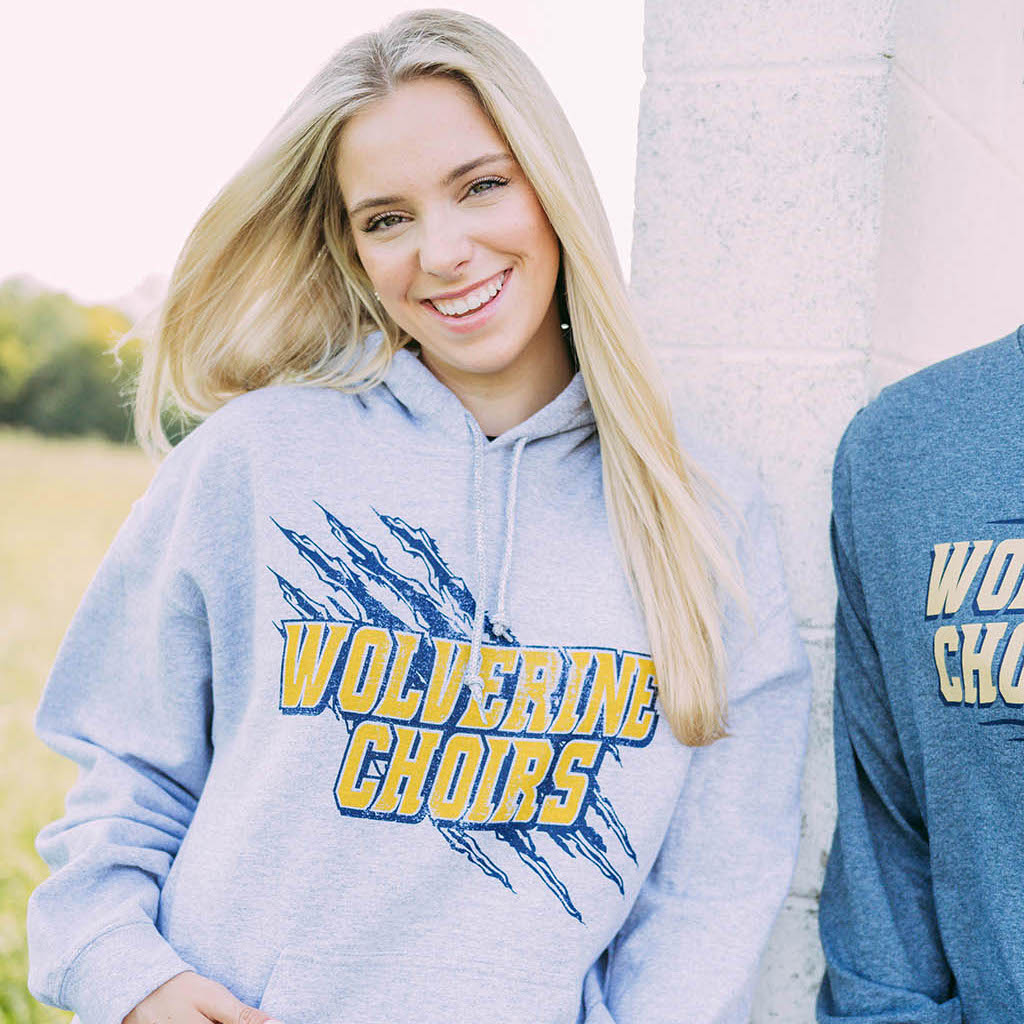 Girl wears light gray hoodie with claw marks and "Wolverine Choirs" written across it.